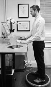 Chiropractor Andrew Harlow shows example of varied posture by standing on a balance board at the desk